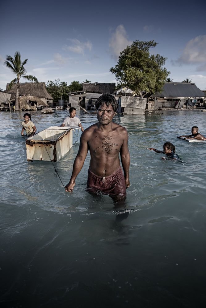 Uma família atravessa sua aldeia inundada, recolhendo pedras para construir um muro de contenção da água do mar em Tarawa, no Kiribati.