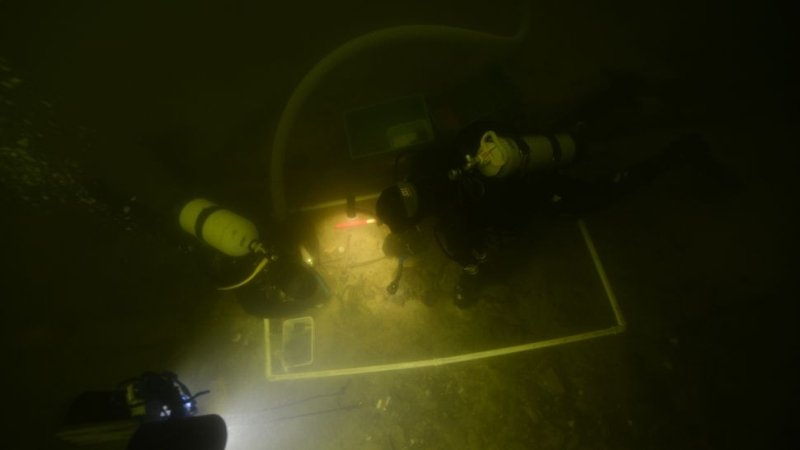 Arqueólogos e mergulhadores trabalham na remoção do corpo e dos artefatos
